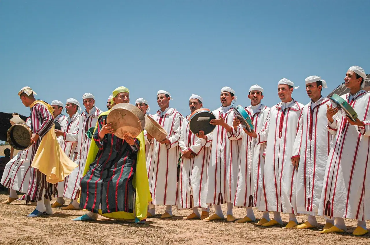 Amazigh musicians in white djellabas playing bendir drums at an outdoor ceremony