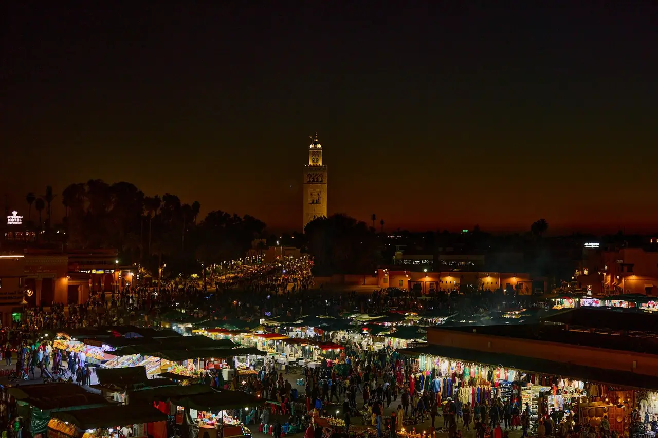 Crowds and food stalls filling Jemaa el-Fna square in Marrakech at night, the Koutoubia minaret beyond
