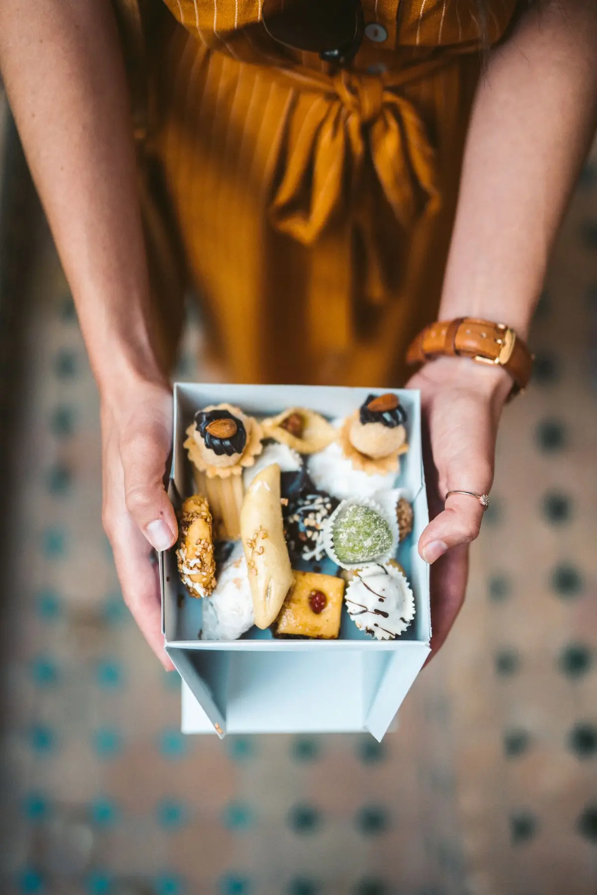 Woman holding a gift box of assorted Moroccan pastries — almond, coconut and sesame sweets