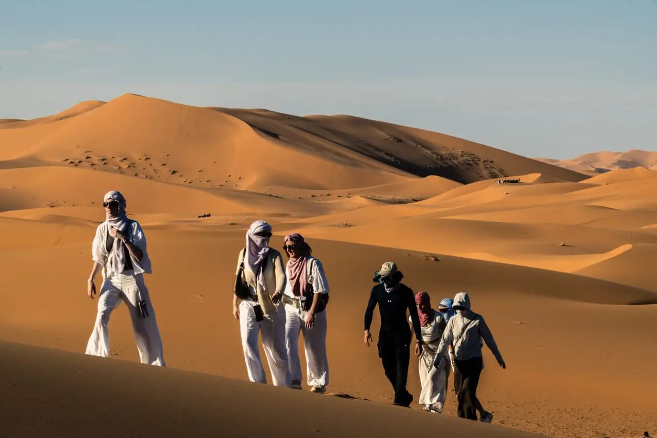 Trekkers climbing the crest of a tall Sahara dune near Merzouga