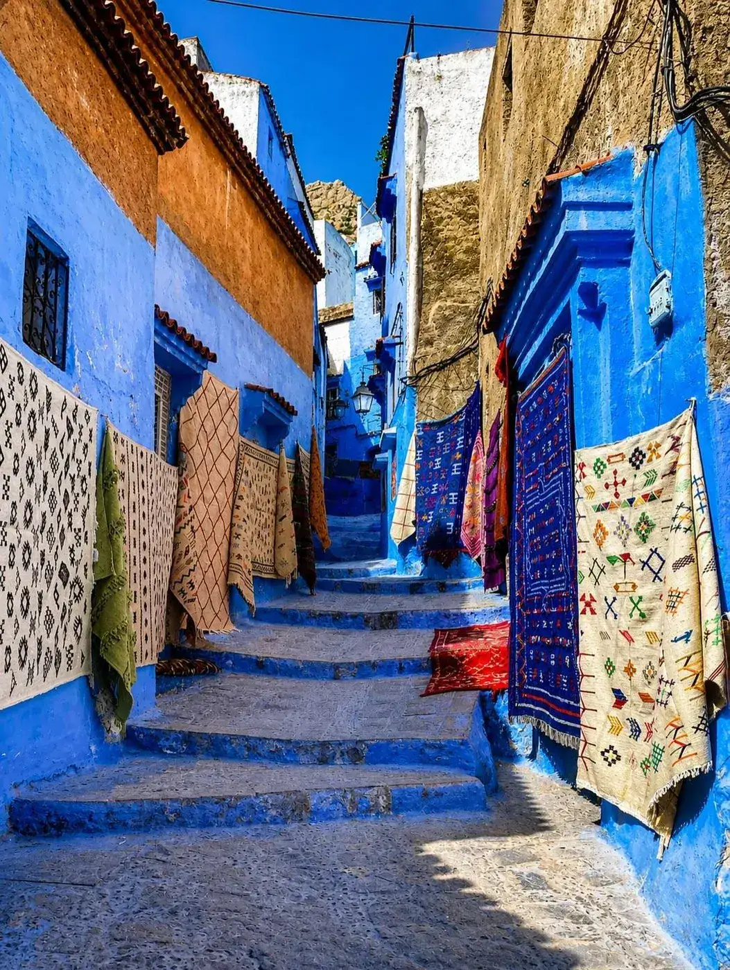 Blue-washed street lined with Berber carpets for sale in the Chefchaouen medina, Morocco