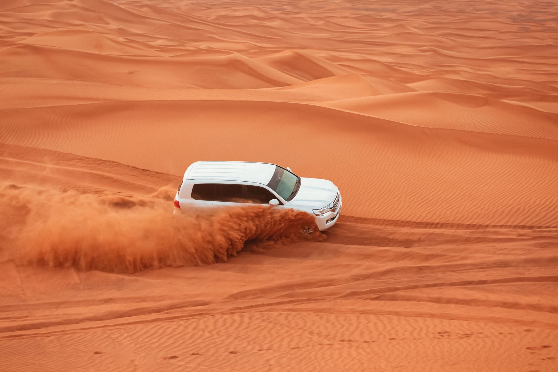 White 4x4 SUV performing dune bashing in the orange Sahara Desert