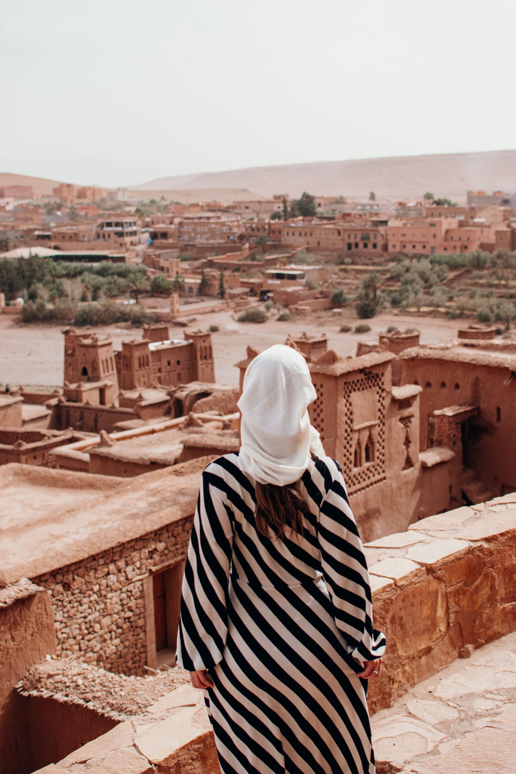 Tourist in a striped robe overlooking the ancient Ait Ben Haddou ksar from a rooftop
