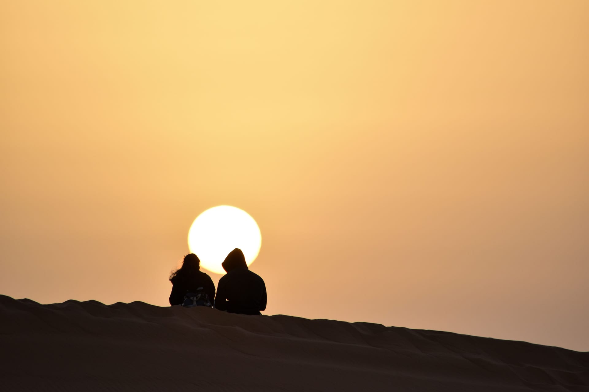 Silhouette of a couple watching sunset from an Erg Chebbi dune — romantic Sahara