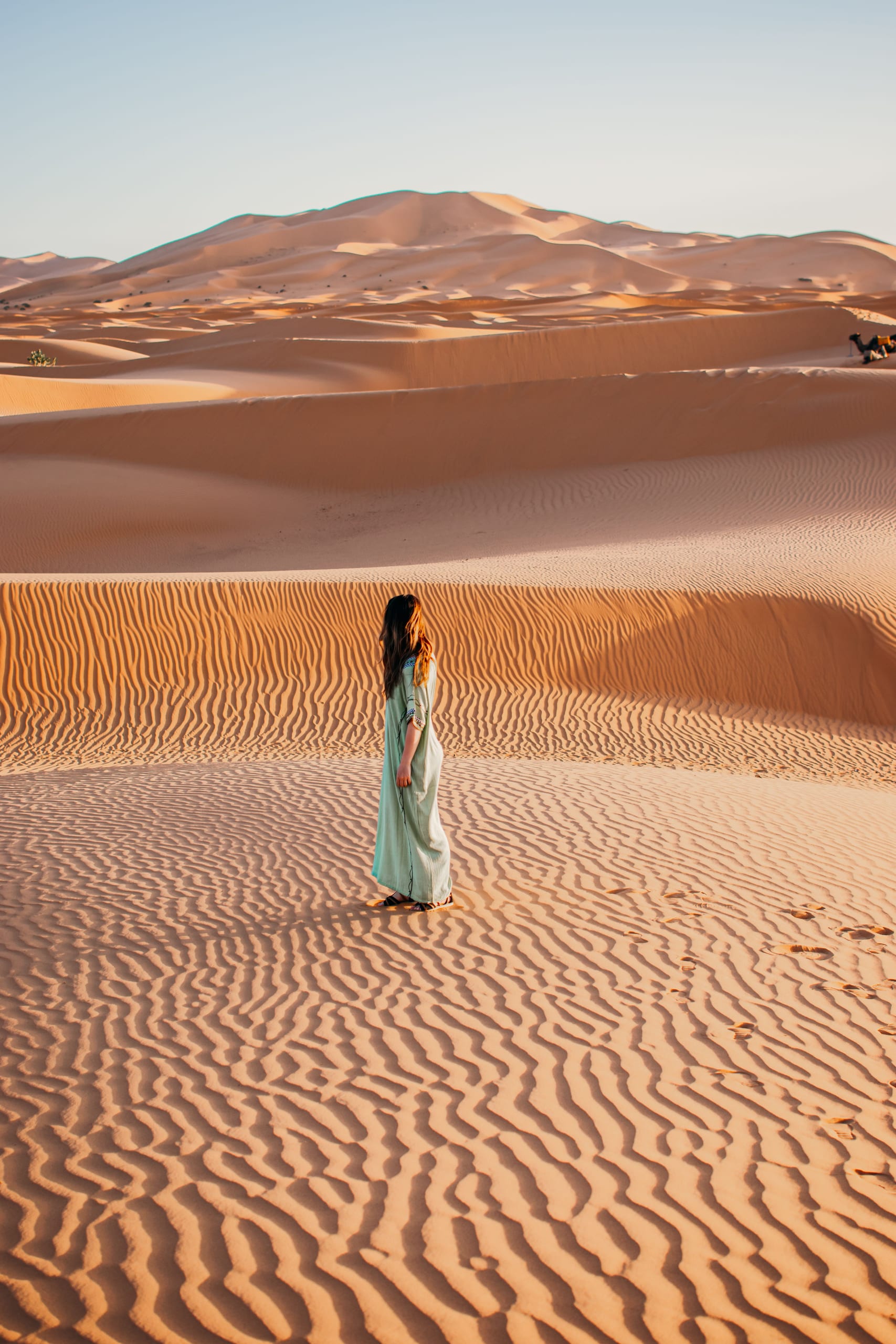 Woman in a teal dress on rippled Erg Chebbi dunes at golden hour