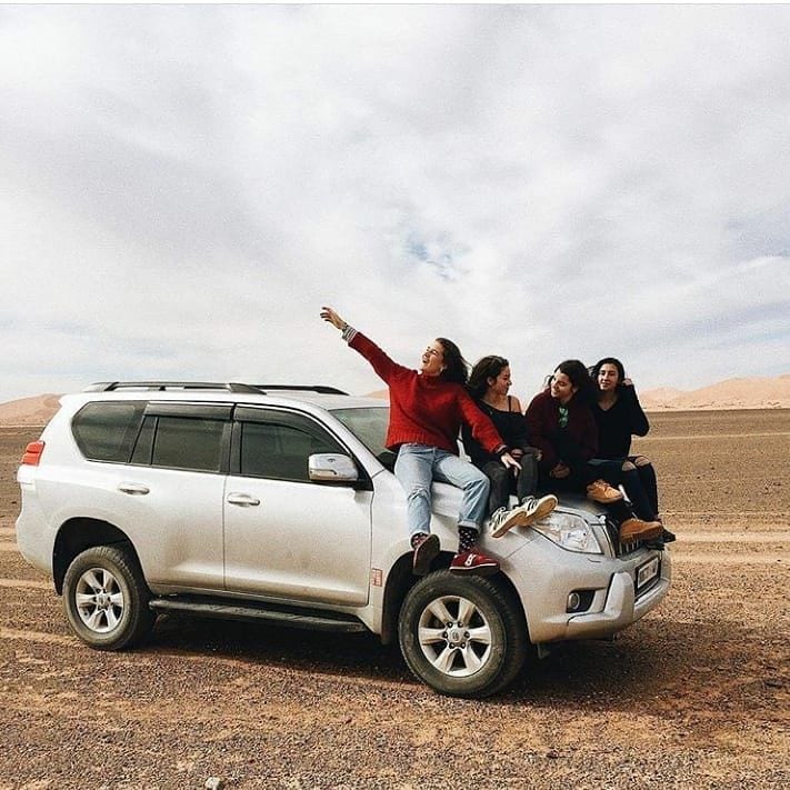 Four female friends posing on a silver Land Cruiser hood — private desert road trip