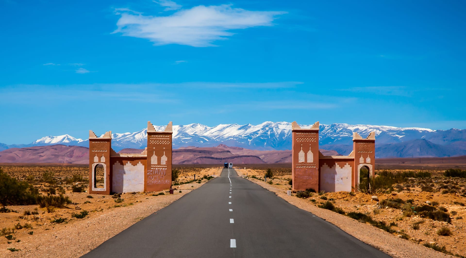 Moroccan kasbah gateway on a desert road with snow-capped High Atlas behind