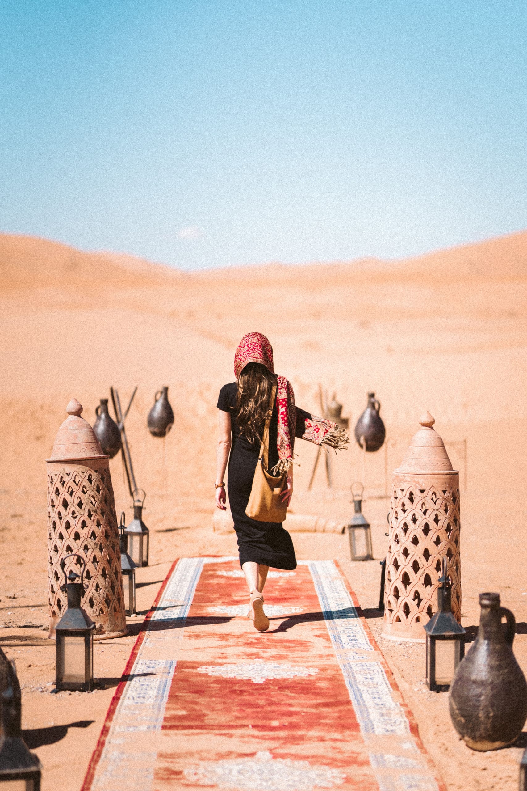 Tourist walking on a Moroccan rug lined with lanterns toward Erg Chebbi — luxury camp entrance