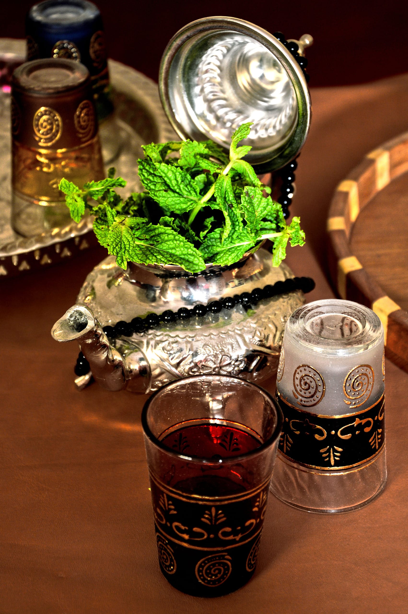 Traditional Moroccan mint tea in ornate gold-decorated glasses beside a silver teapot