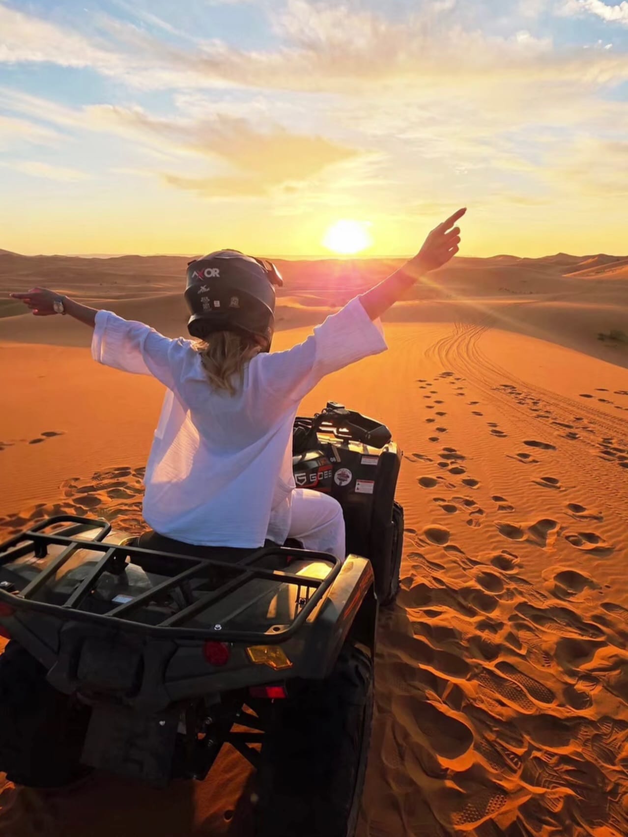 Female tourist with arms outstretched on a quad bike at sunset at Erg Chebbi