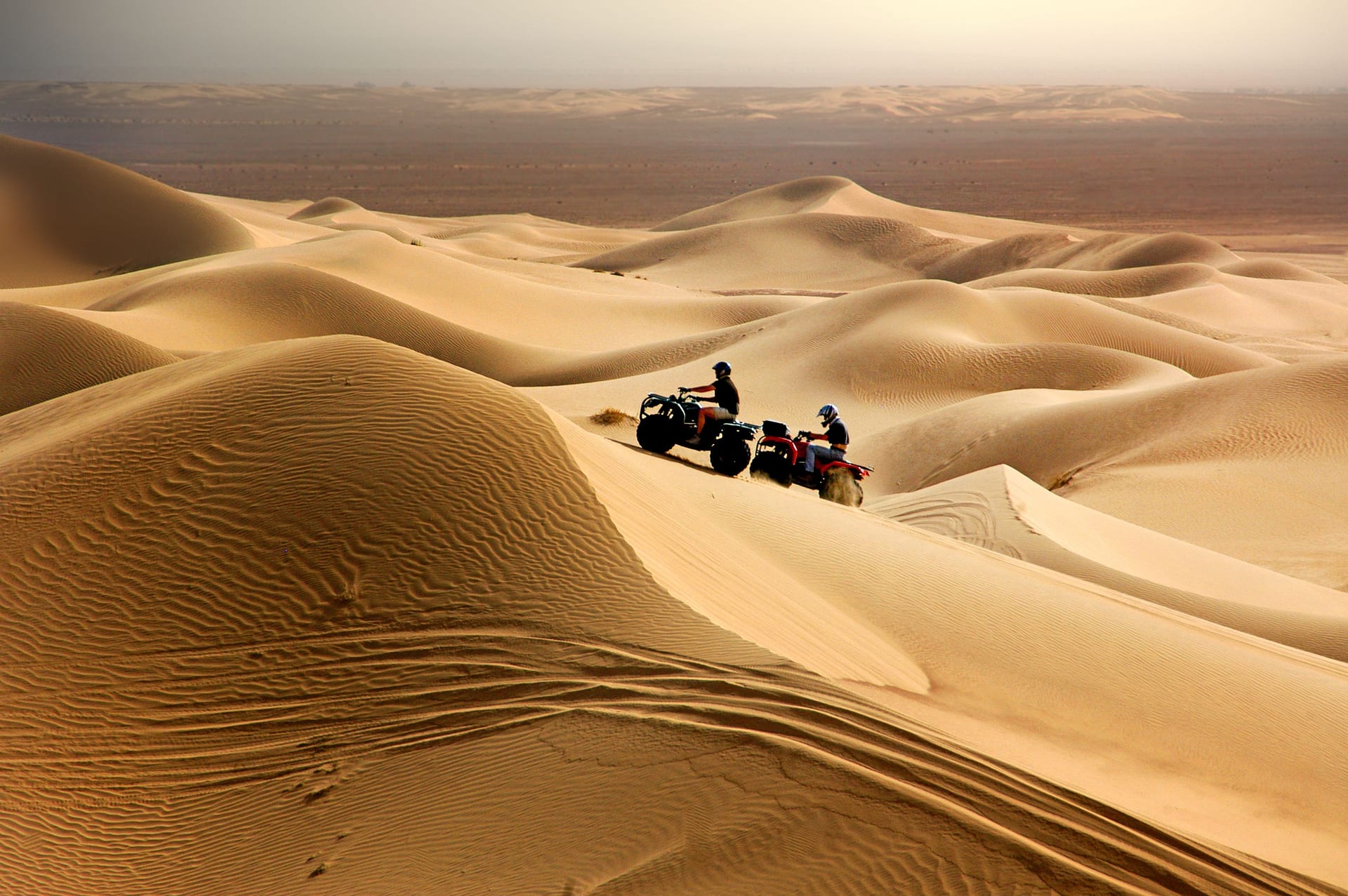 Two quad bikers crossing pale Sahara dunes