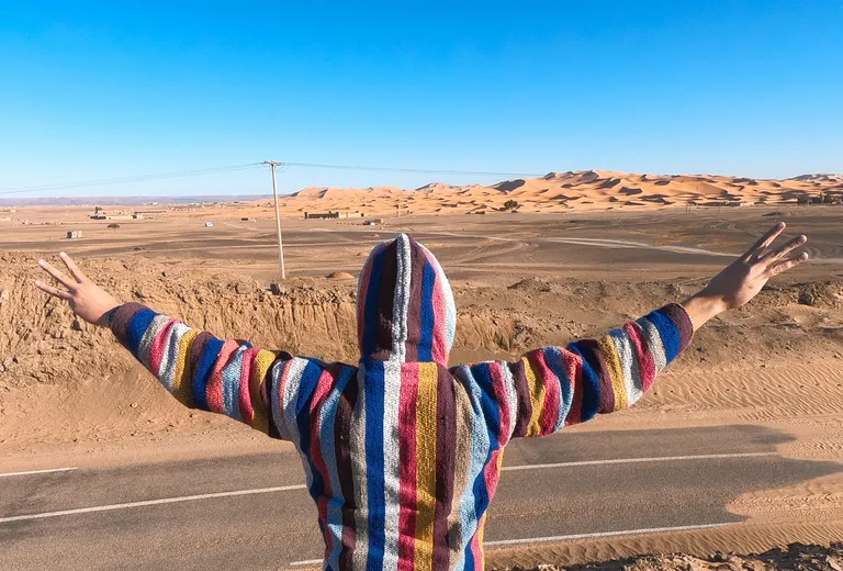 Tourist in a colourful Moroccan djellaba facing the Erg Chebbi dune sea near Merzouga
