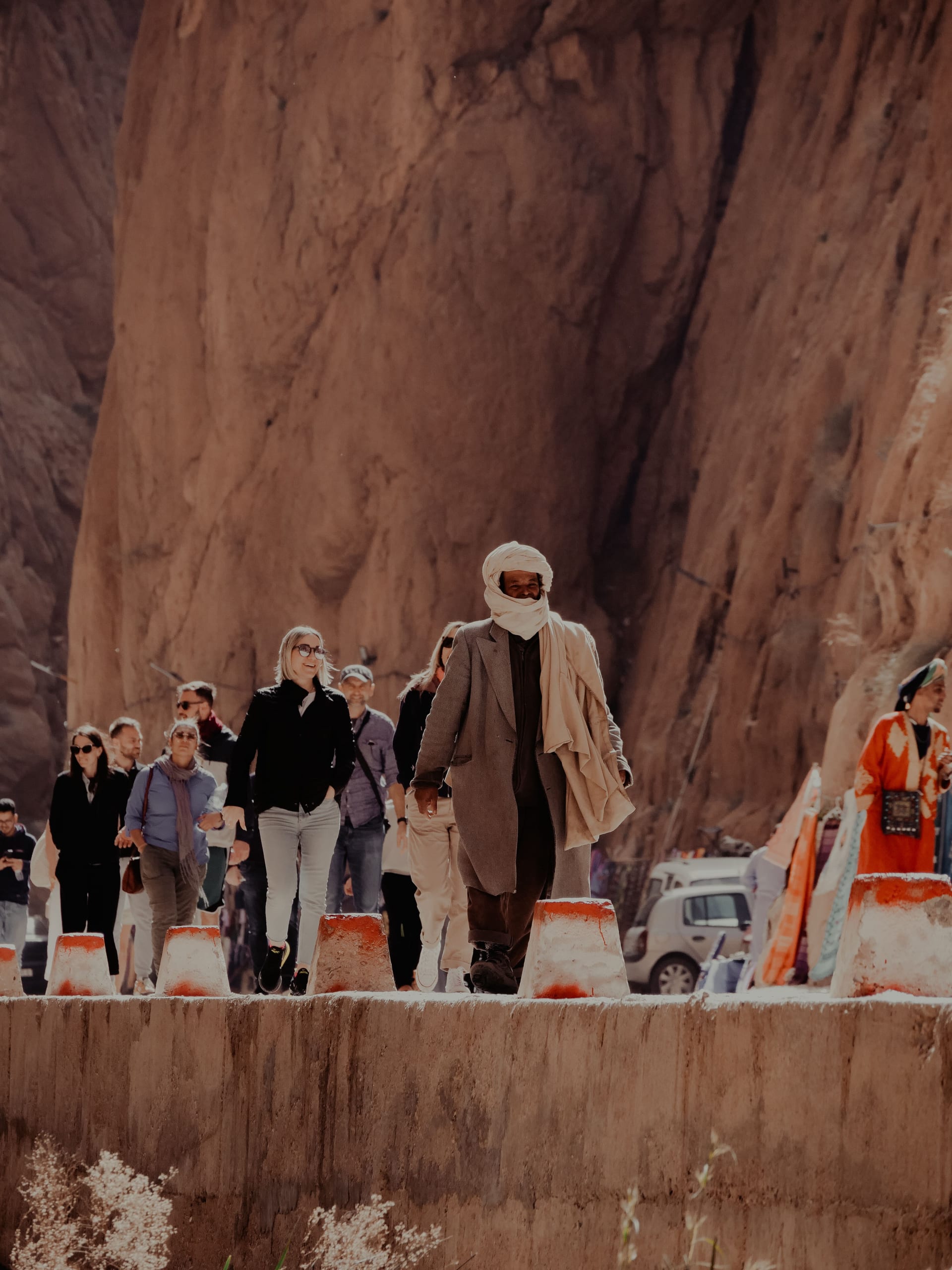 Group of tourists walking through Todra Gorge with a Berber guide — red limestone cliffs