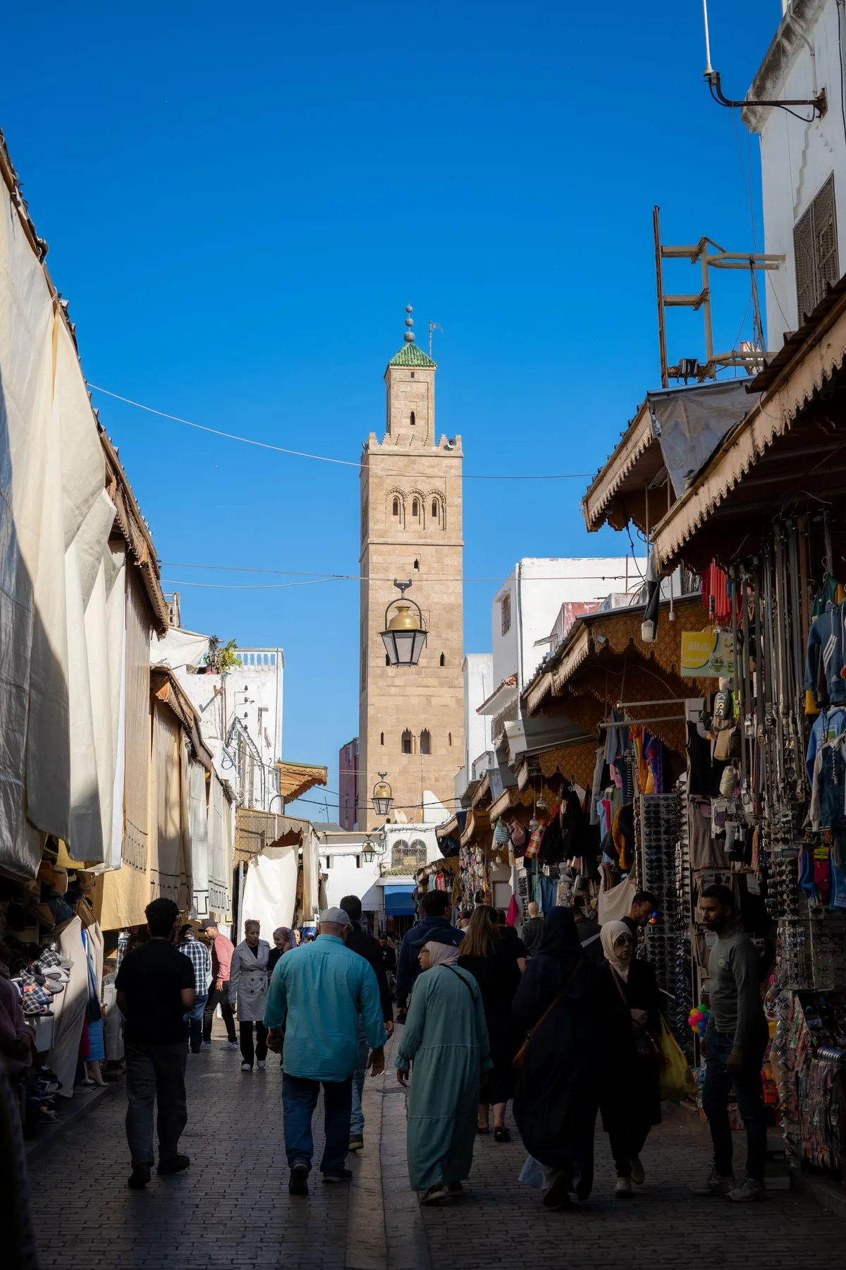 A narrow souk alley in Marrakech lined with market stalls, leading toward a minaret