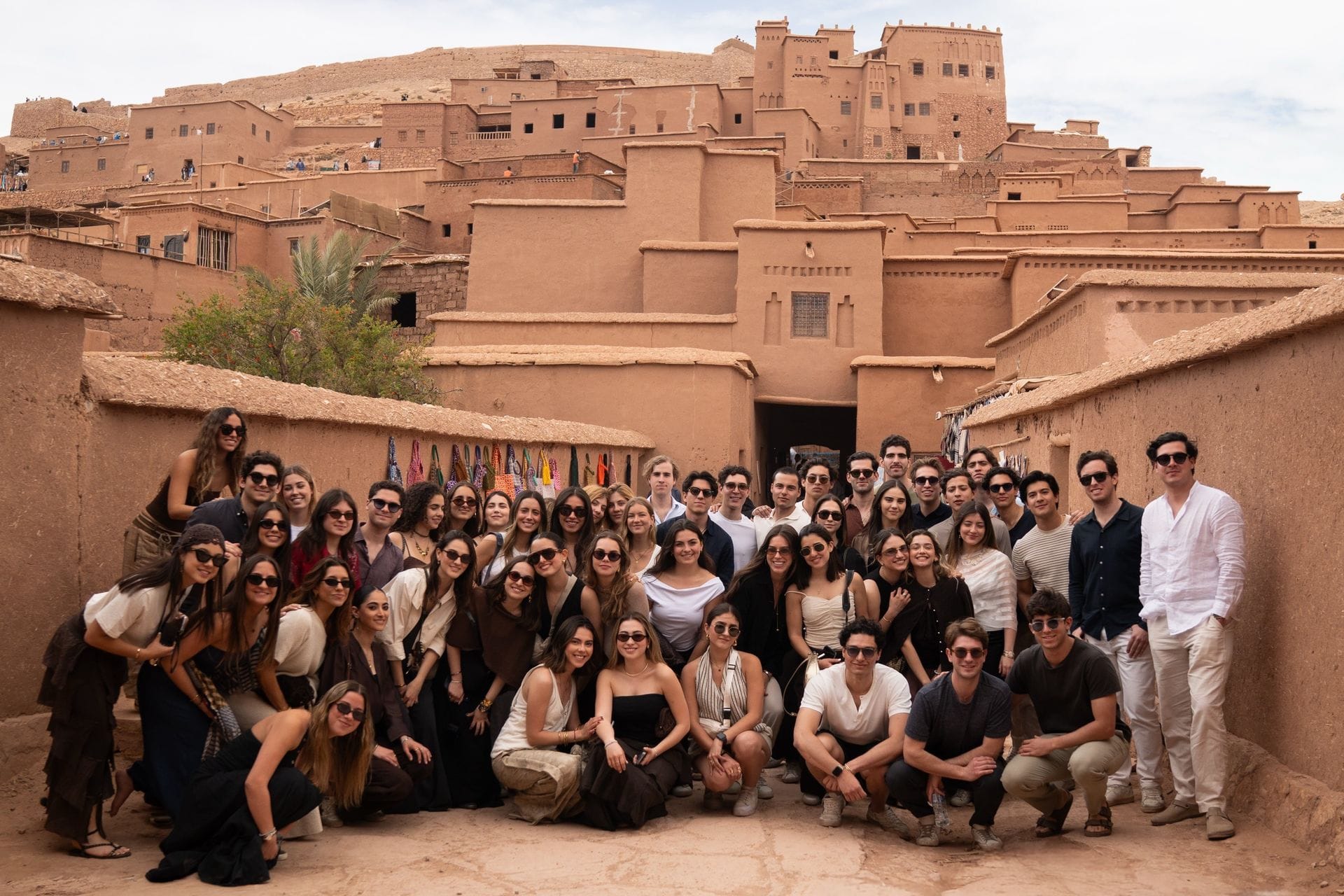 Large student group gathered in an earthen lane at the entrance to Aït Ben Haddou