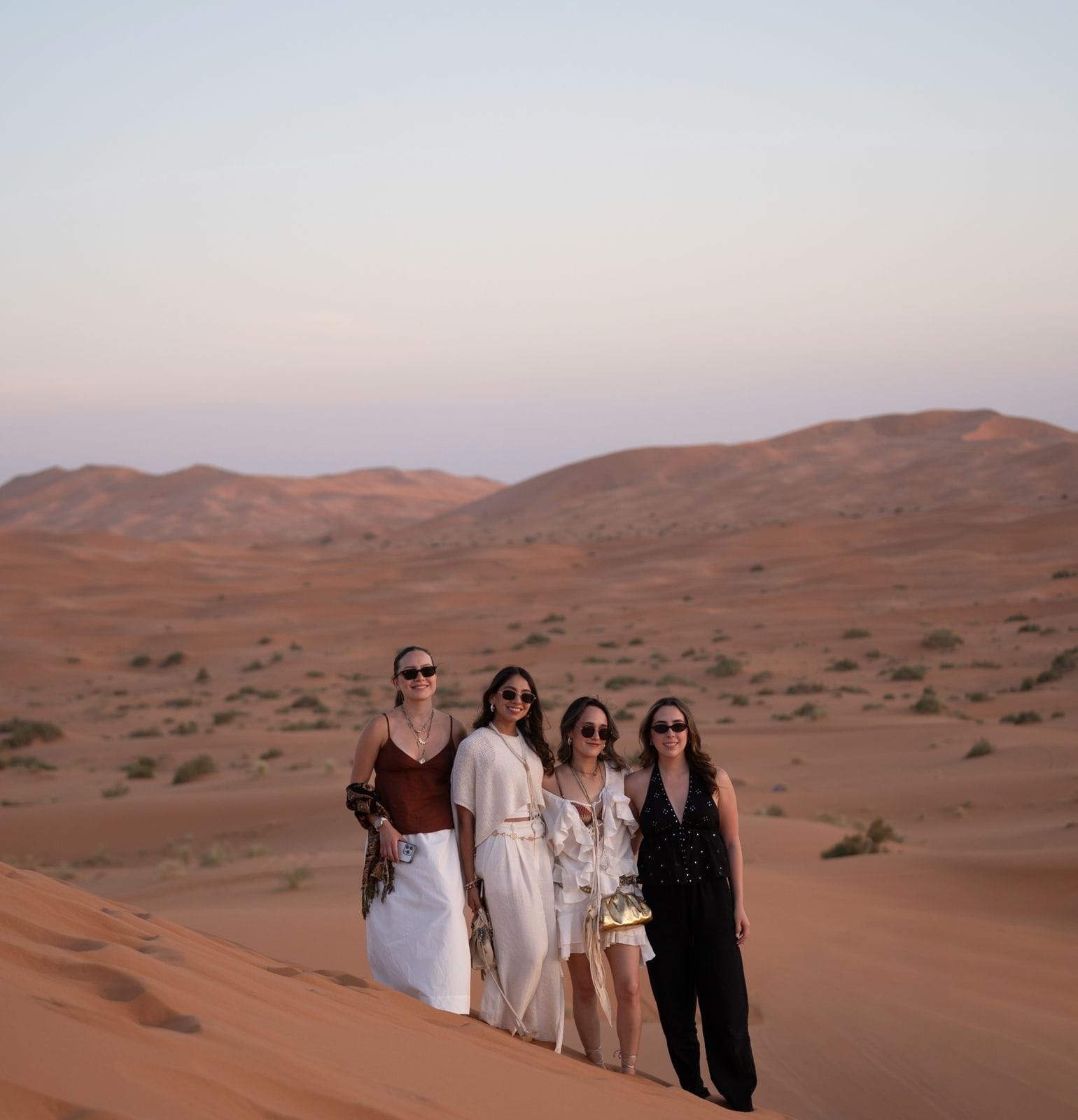 Four students standing on a sand dune in the evening light